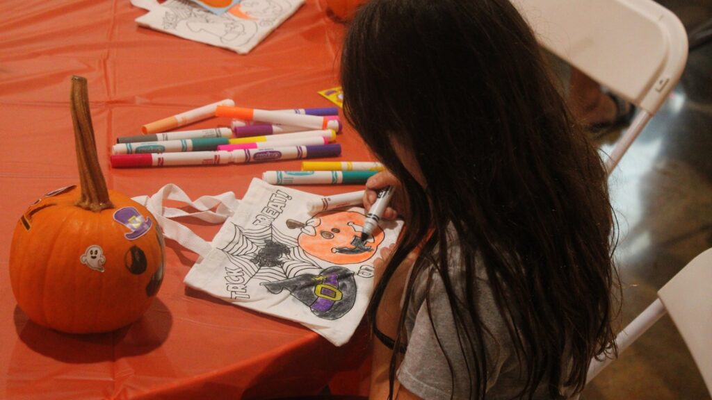 A child colouring a paper trick-or-treat bag at the craft table