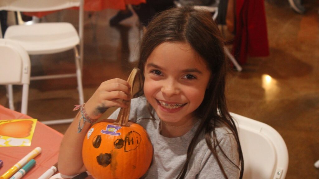 A girl holding up the pumpkin she decorated