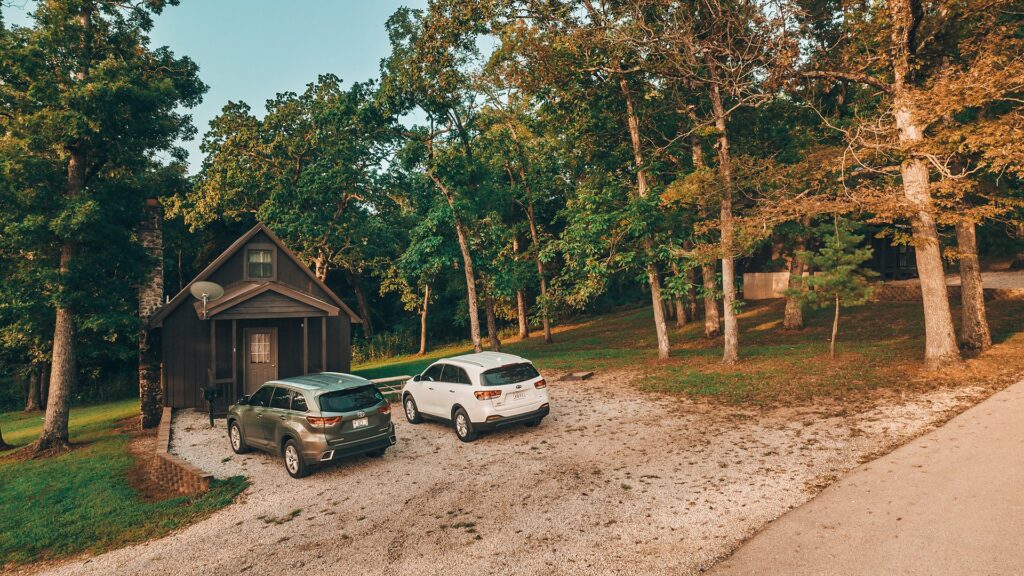 A cabin set back among the oaks with guest cars parked on the gravel pad.