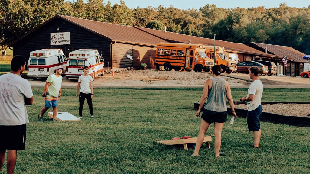 Guests playing cornhole on the lawn in the evening, with the office and shuttle buses behind.