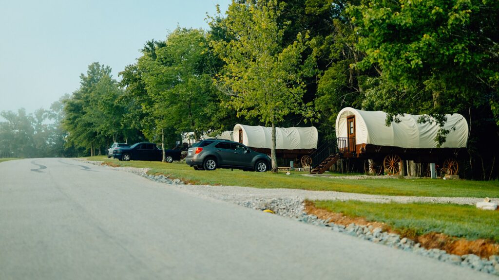 Canvas-topped covered wagons parked in a shaded row beside the road.