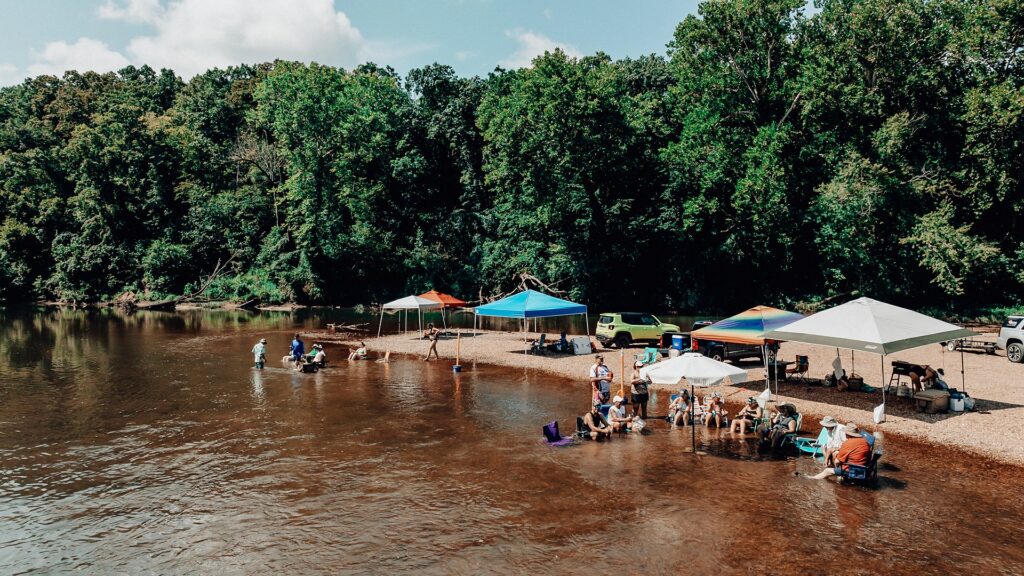 Families under shade canopies along the river beach.