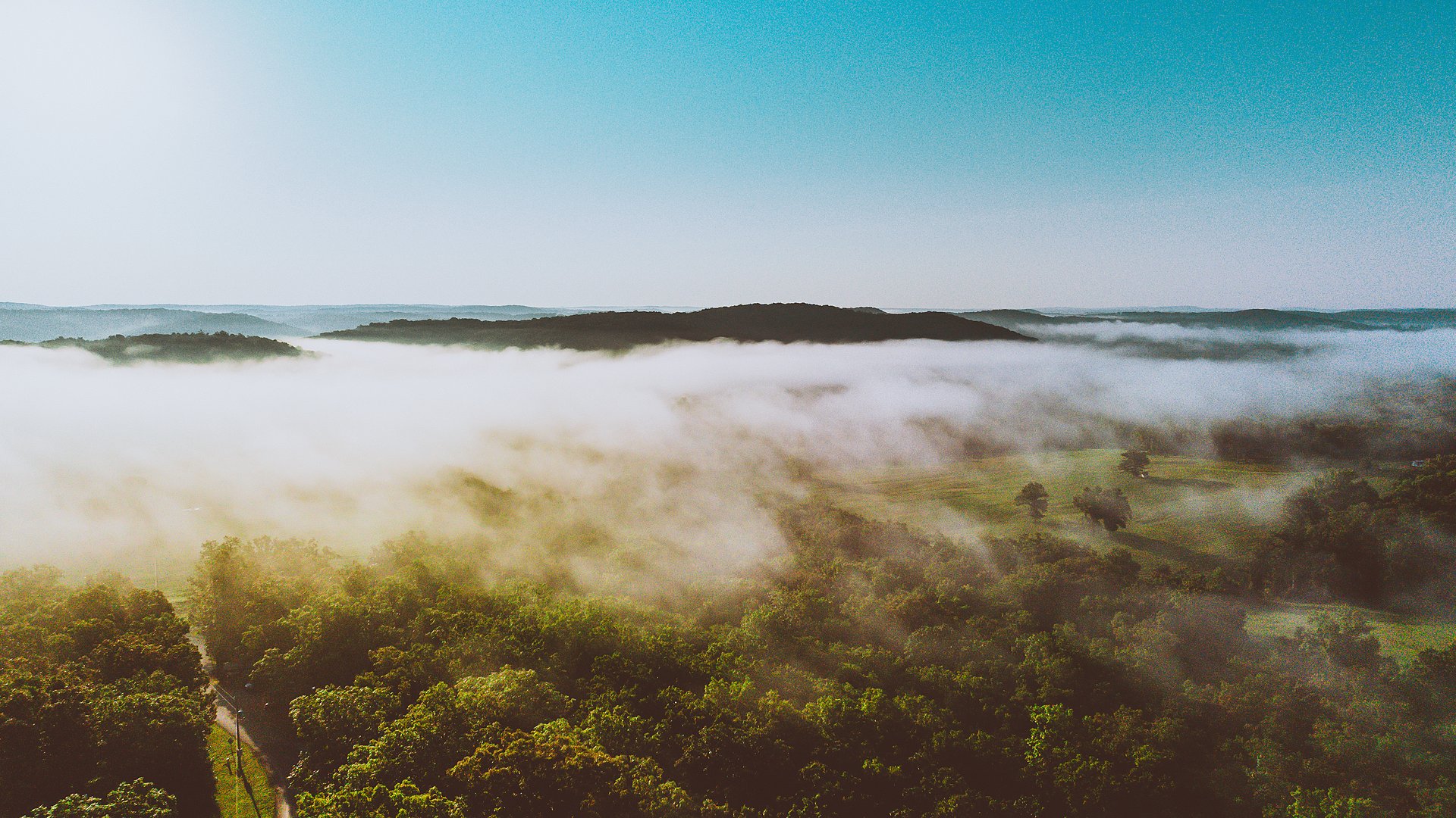 Morning fog filling the valley between wooded Ozark hills, seen from the air.