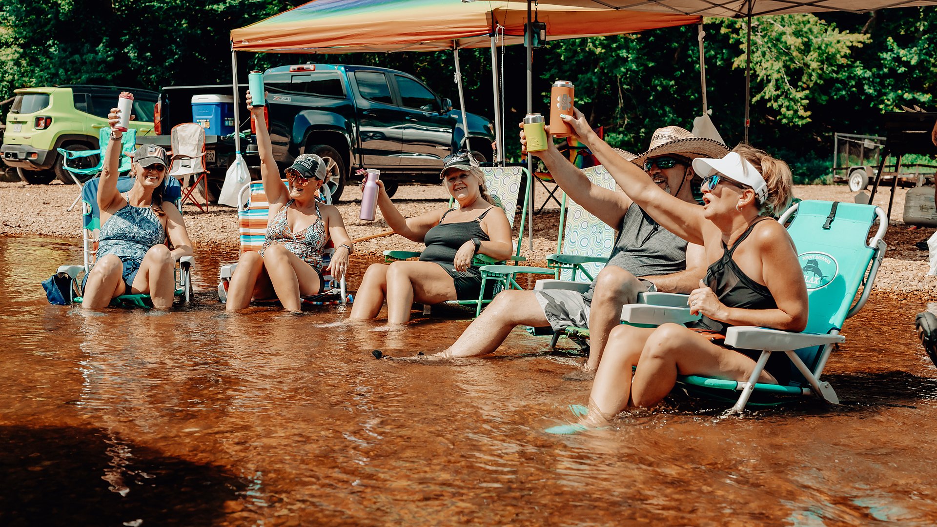 A group of friends toasting in their chairs at the river's edge.