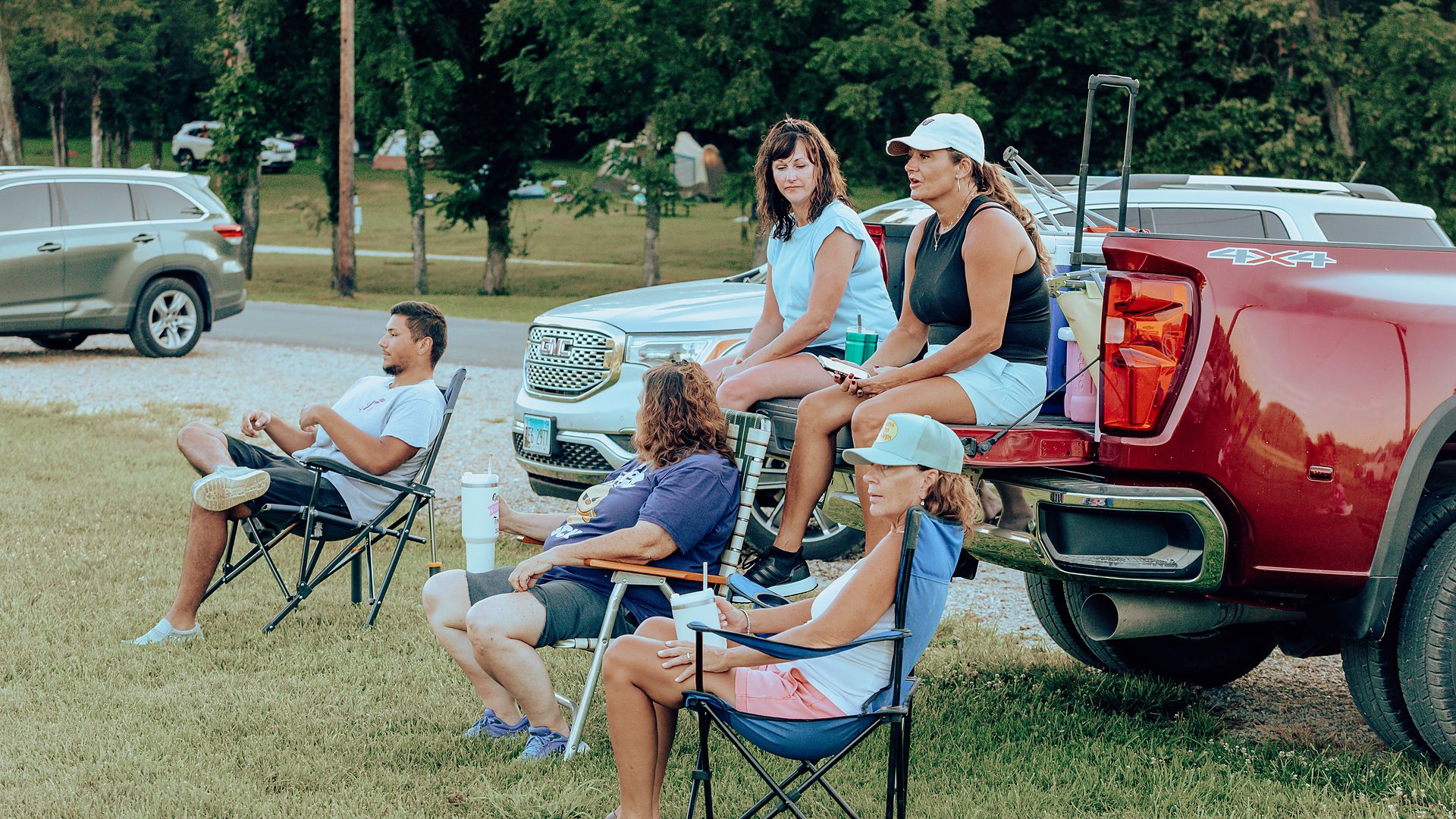 Guests relaxing in camp chairs around a pickup tailgate at their site.