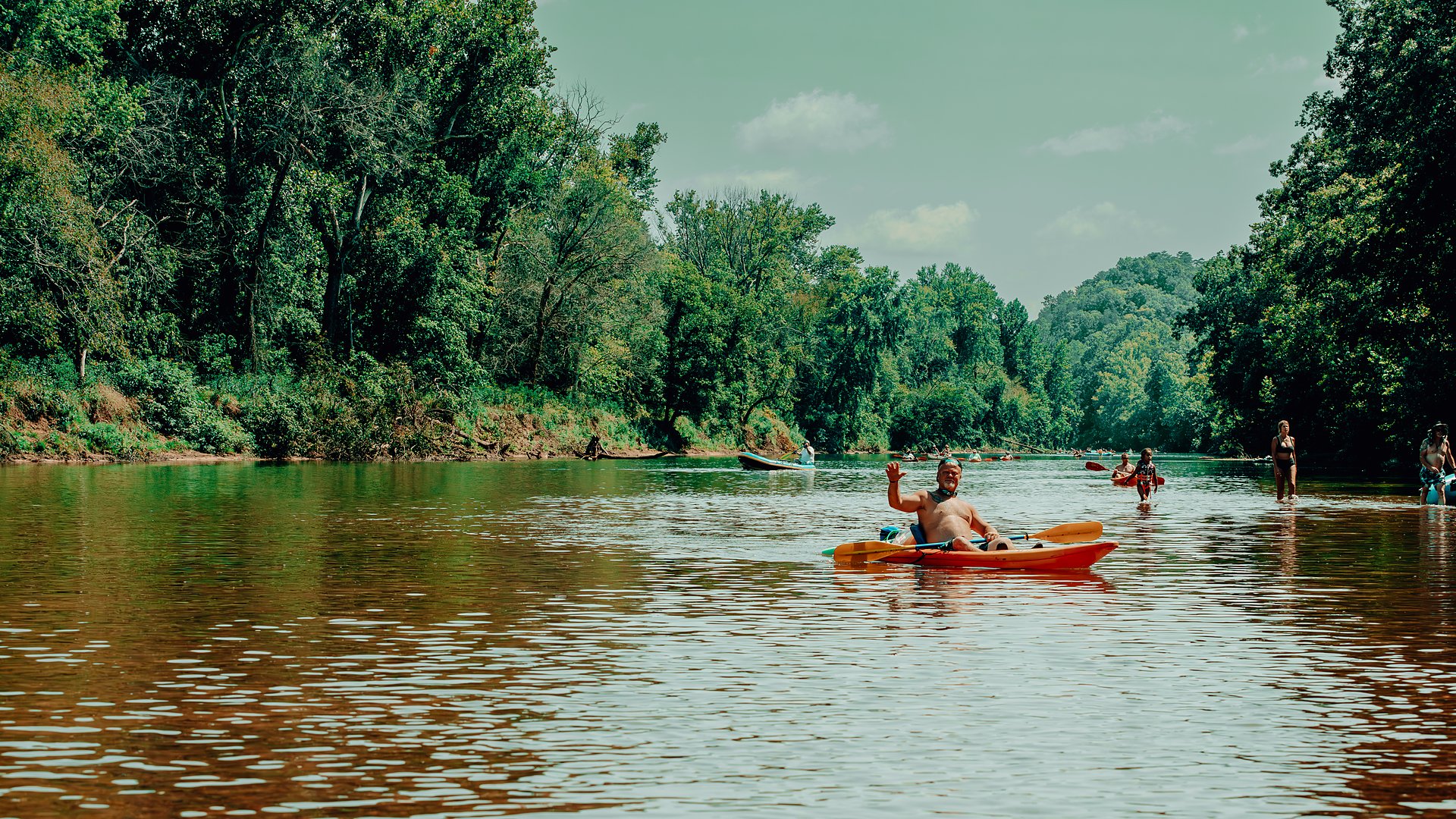 A kayaker waving as they paddle down the middle of the river.