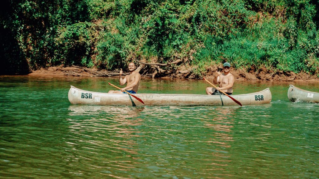 Two guests paddling canoes side by side down the river.