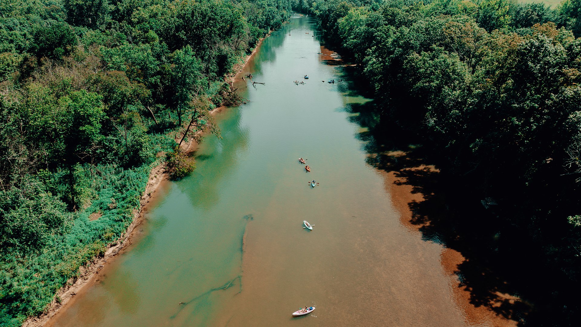 An aerial view down the Meramec with floaters spread along the green water.