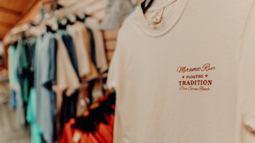 A cream T-shirt printed 'Meramec River Floating Tradition' on the camp store rack.