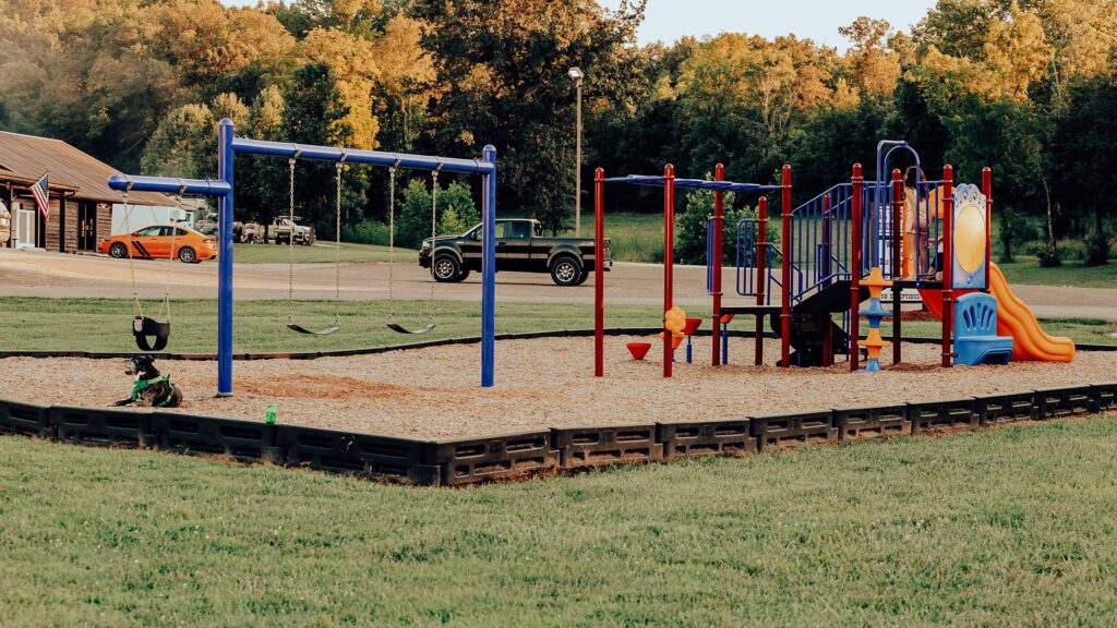 The campground playground with swings and a climbing frame on a bed of mulch.