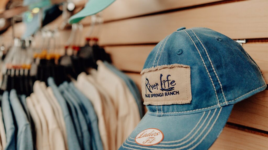 A denim 'River Life' cap on display among the clothing racks.