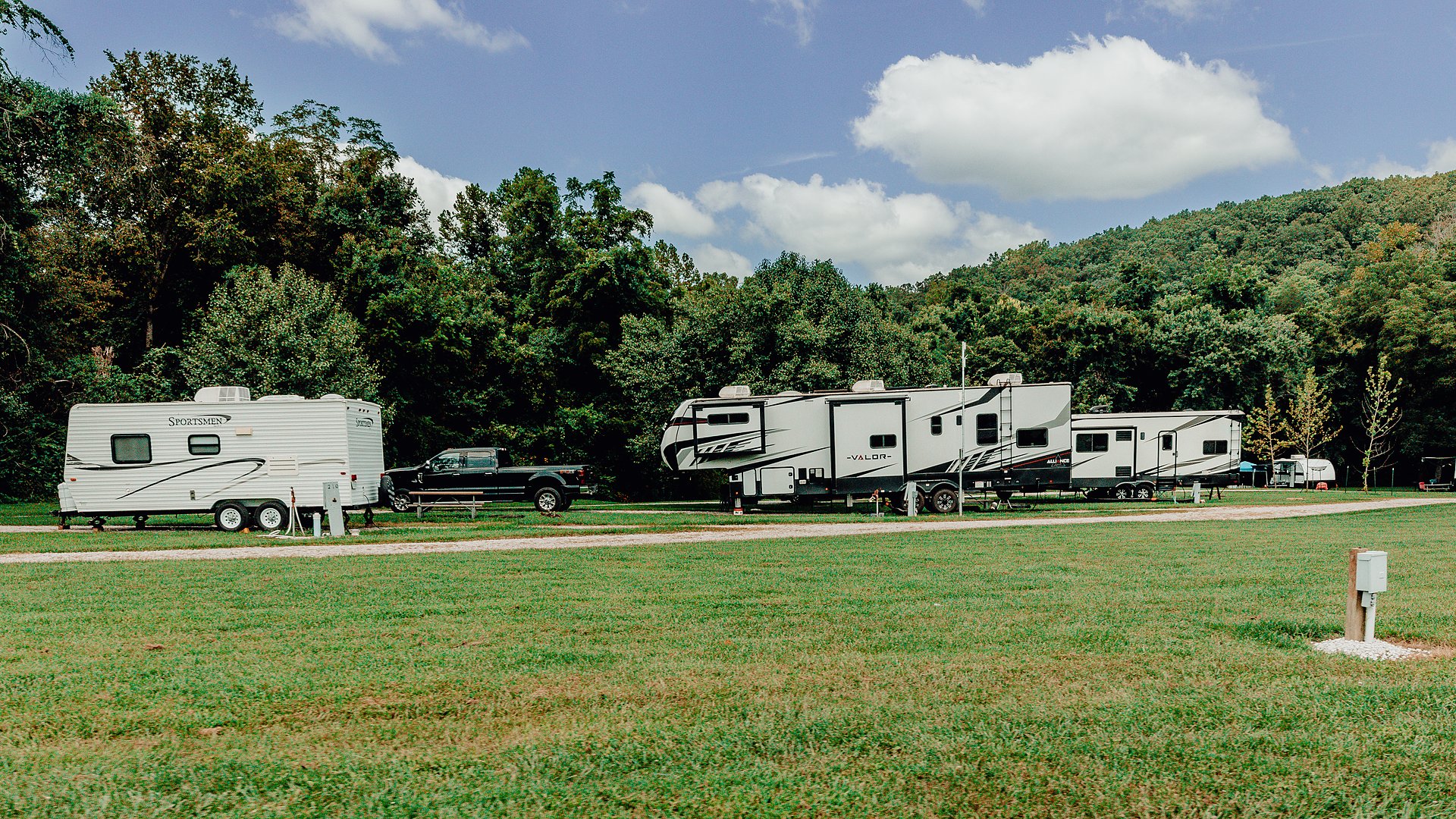Travel trailers on full-hookup RV sites with the wooded ridge behind.