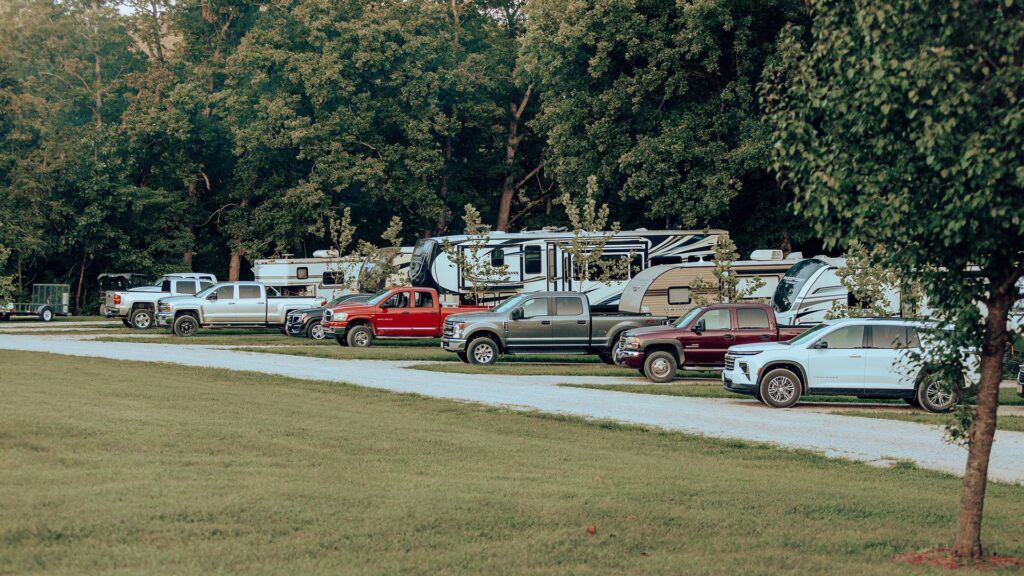 Travel trailers and pickup trucks lined up along the shaded gravel road through the RV sites.