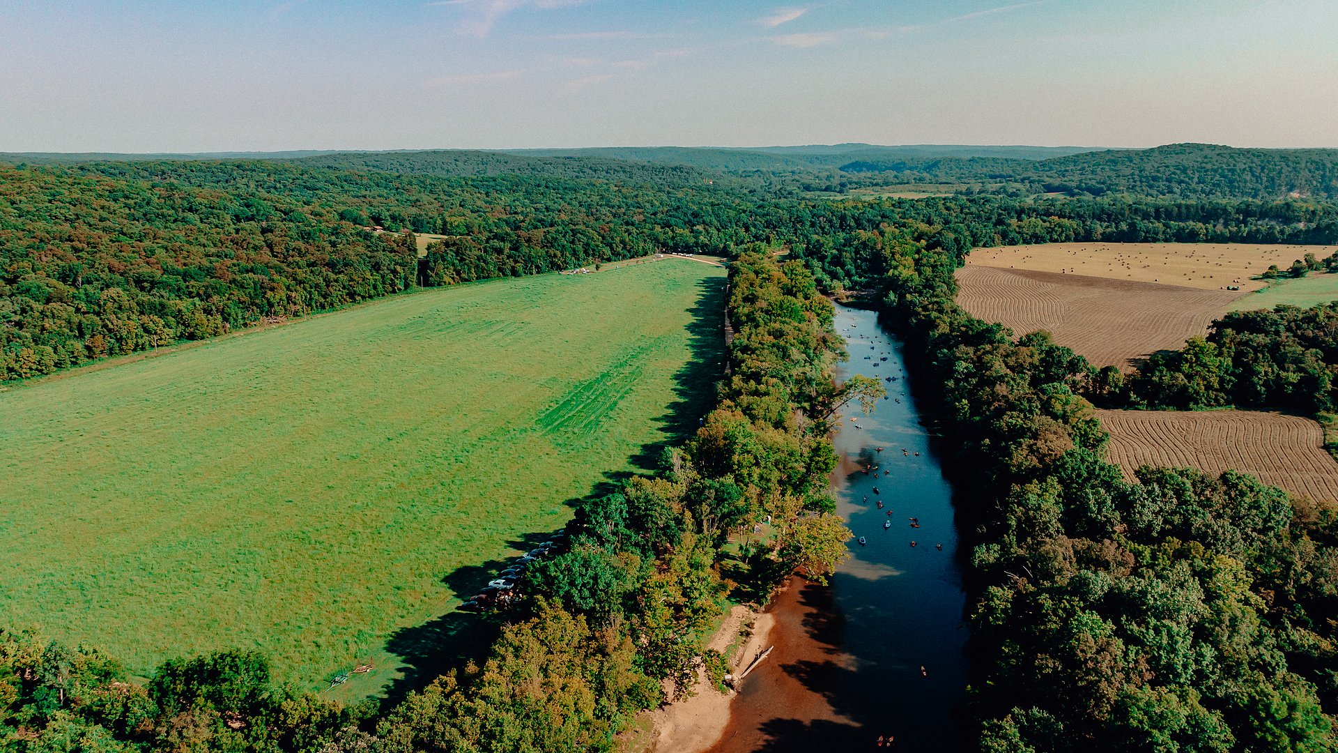 An aerial view of the Upper Meramec running past a green hayfield.