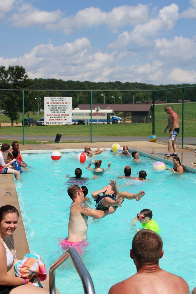 Guests splashing in the swimming pool with beach balls as a child is tossed into the air.