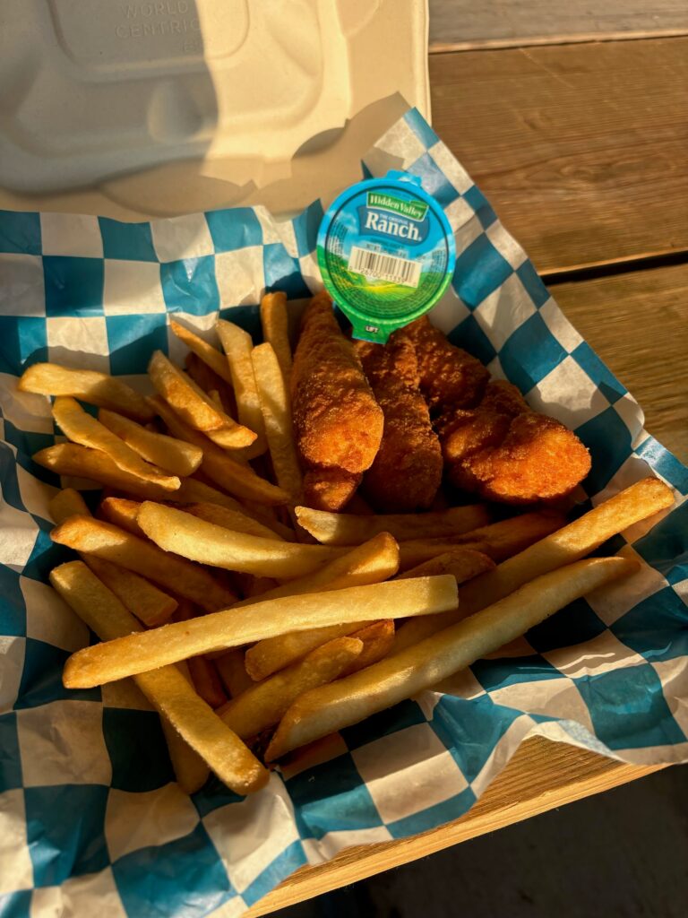 Chicken strips and fries in a checkered paper basket with a cup of ranch dressing.