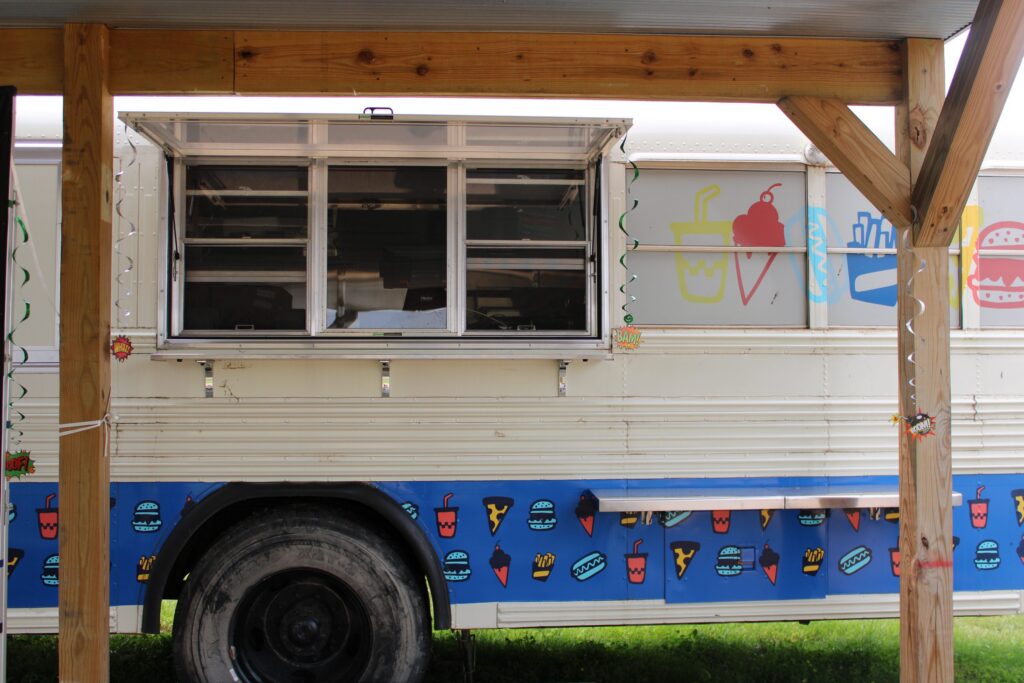 The food truck's serving window under a timber shelter, its side painted with burgers and ice cream.