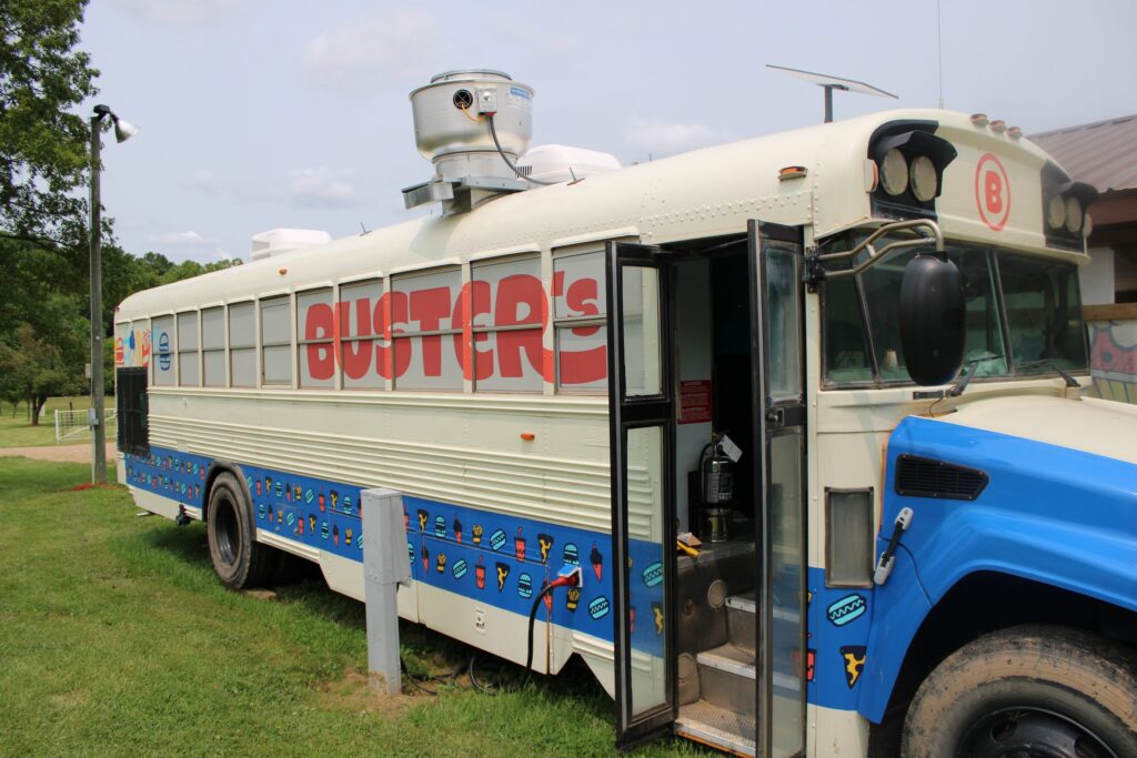 The Buster's food truck, a converted school bus, parked on the grass with its door open.