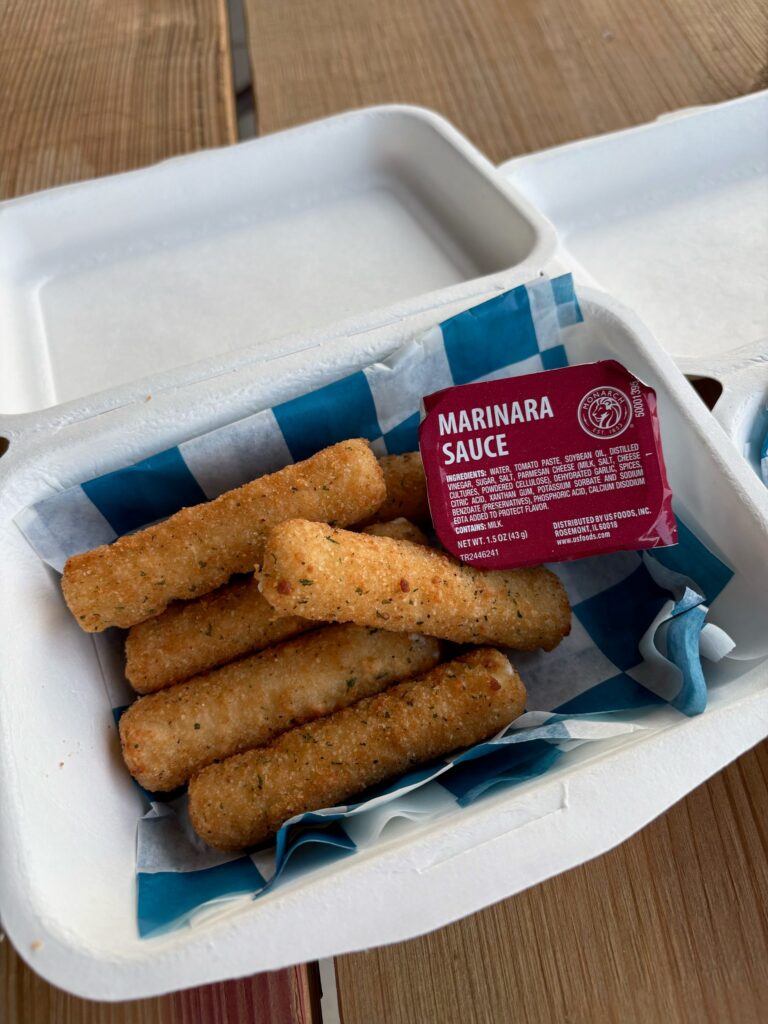 Mozzarella sticks with a packet of marinara sauce in a takeout box.