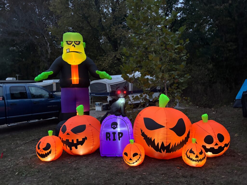 Glowing jack-o'-lantern inflatables and a monster inflatable light up a campsite at dusk.