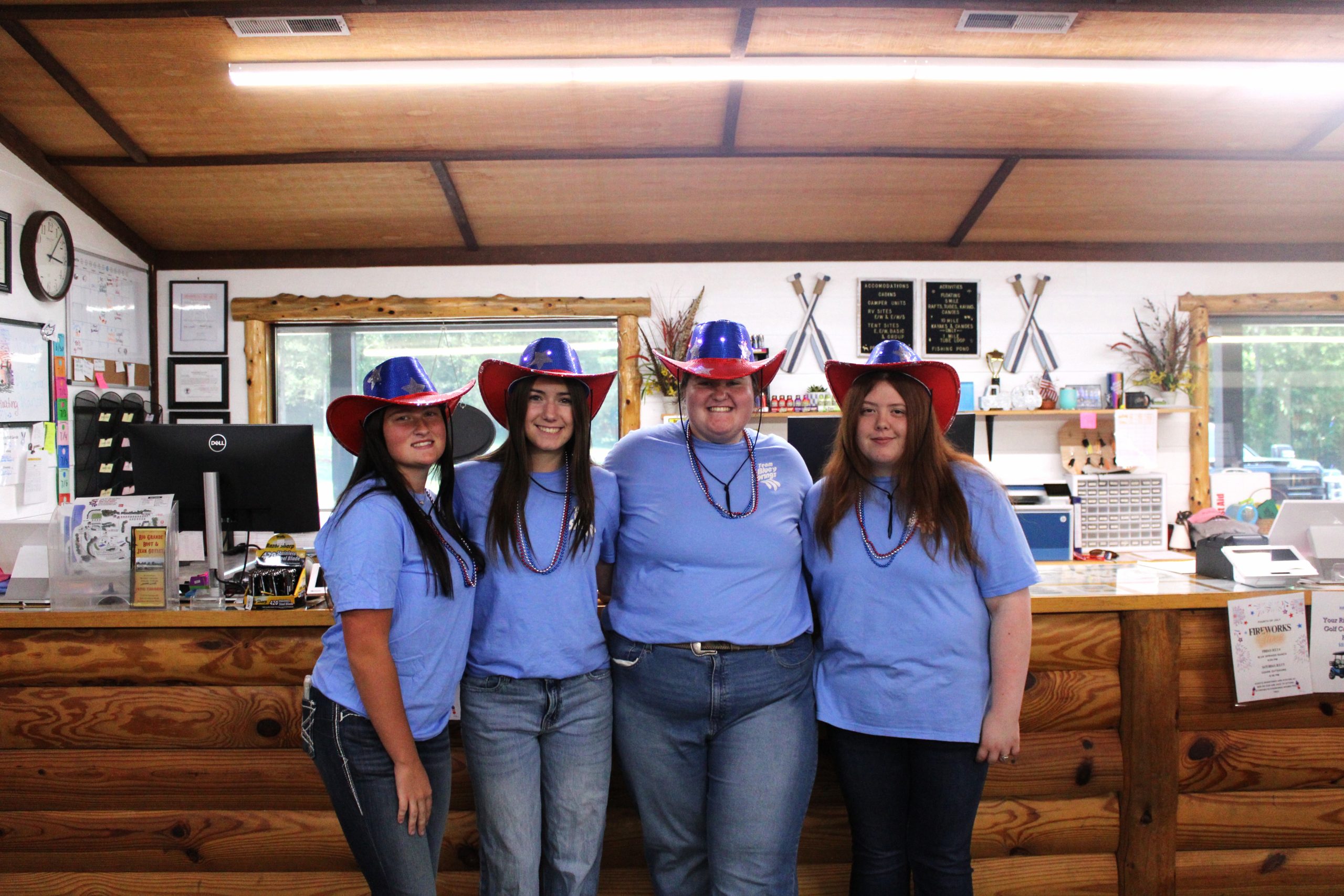 Four staff in matching blue shirts and star-spangled cowboy hats posing in front of the check-in counter.